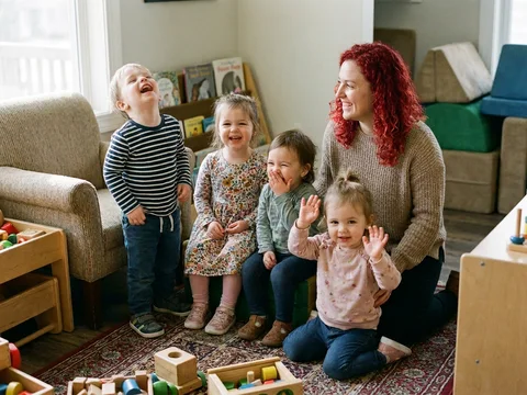 Childcare provider smiling with four children playing together in a playroom
